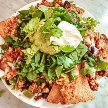 Nachos made with Tofu Taco Meat. Whole grain tortilla chips topped with tofu taco meat, black beans, lettuce, guacamole, Greek yogurt, lettuce and cilantro.