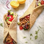 Two Mediterranean chickpea wraps filled with tender marinated chickpeas and fresh vegetables beside lemon and dill.
