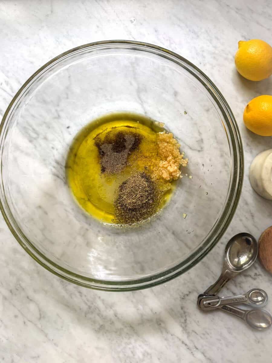 Olive oil, lemon juice, minced garlic, Italian seasoning, salt, and pepper in a glass mixing bowl.