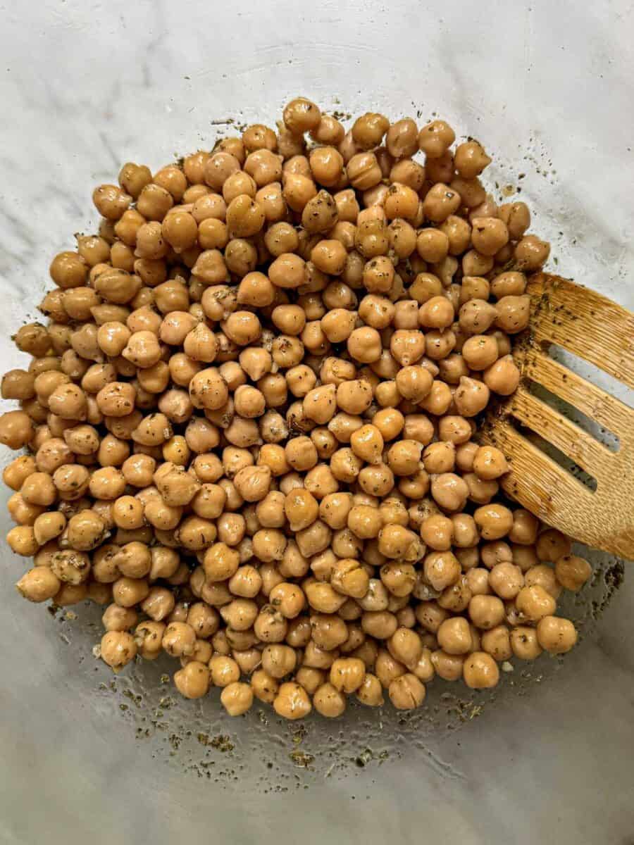 Chickpeas coated in a lemon garlic and Italian herb marinade in a large mixing bowl.