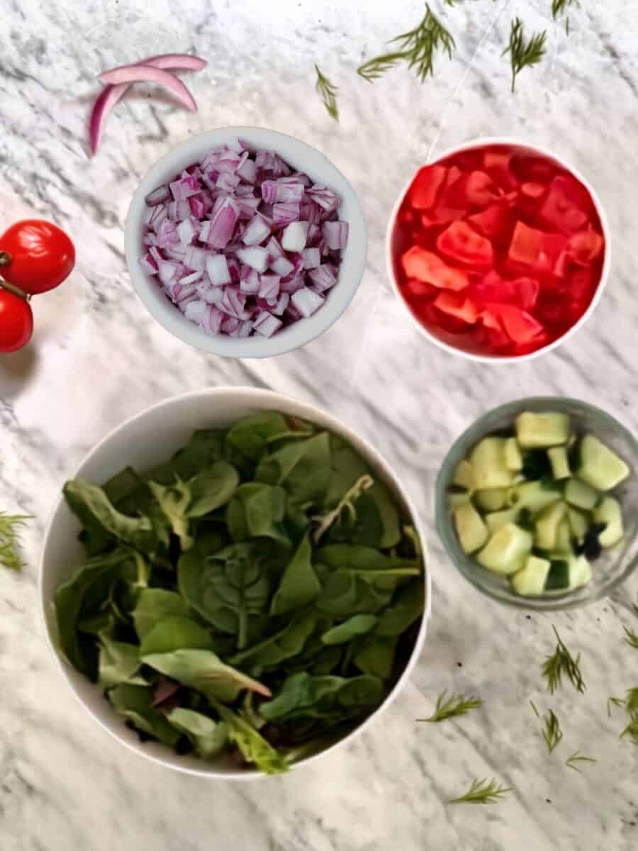 Chopped red onion, tomatoes, cucumber, mixed greens, and fresh dill prepared for chickpea wraps.