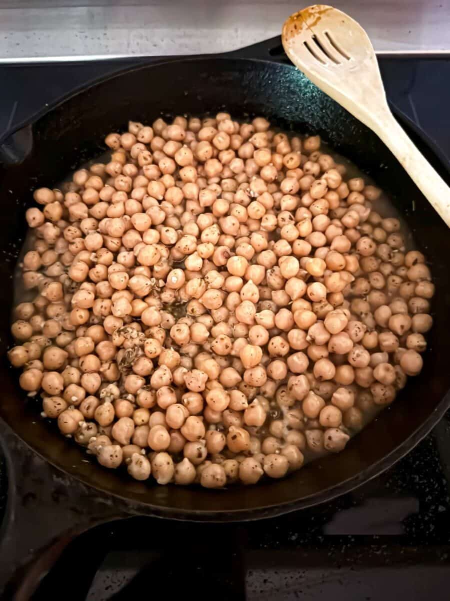 Marinated chickpeas cooking with lemon garlic marinade in a skillet on the stovetop.