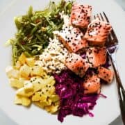 Cooked salmon poke bowl with brown rice, mango, seaweed salad, sesame ginger cabbage, and sesame seeds.