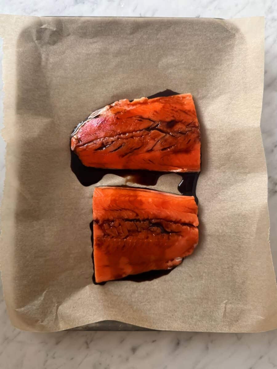 Baked salmon fillets on a parchment-lined baking sheet topped with lite soy sauce.