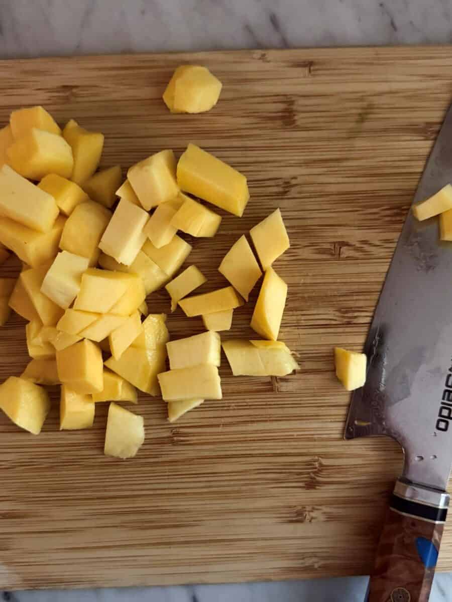 Fresh mango cut into bite-size pieces on a wooden cutting board.