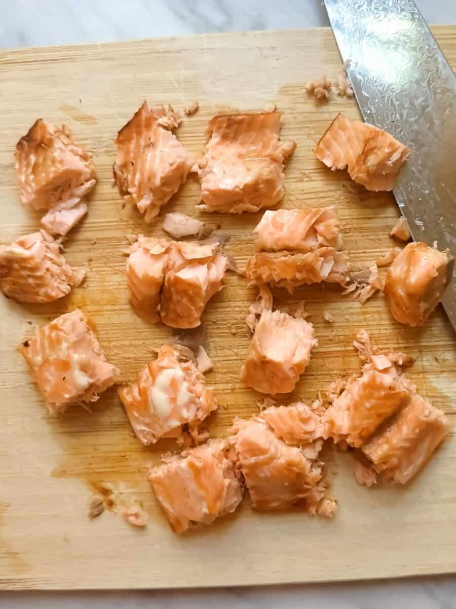 Salmon chopped into cubes for cooked salmon poke bowls. Cubes are resting on a cutting board with a knife.