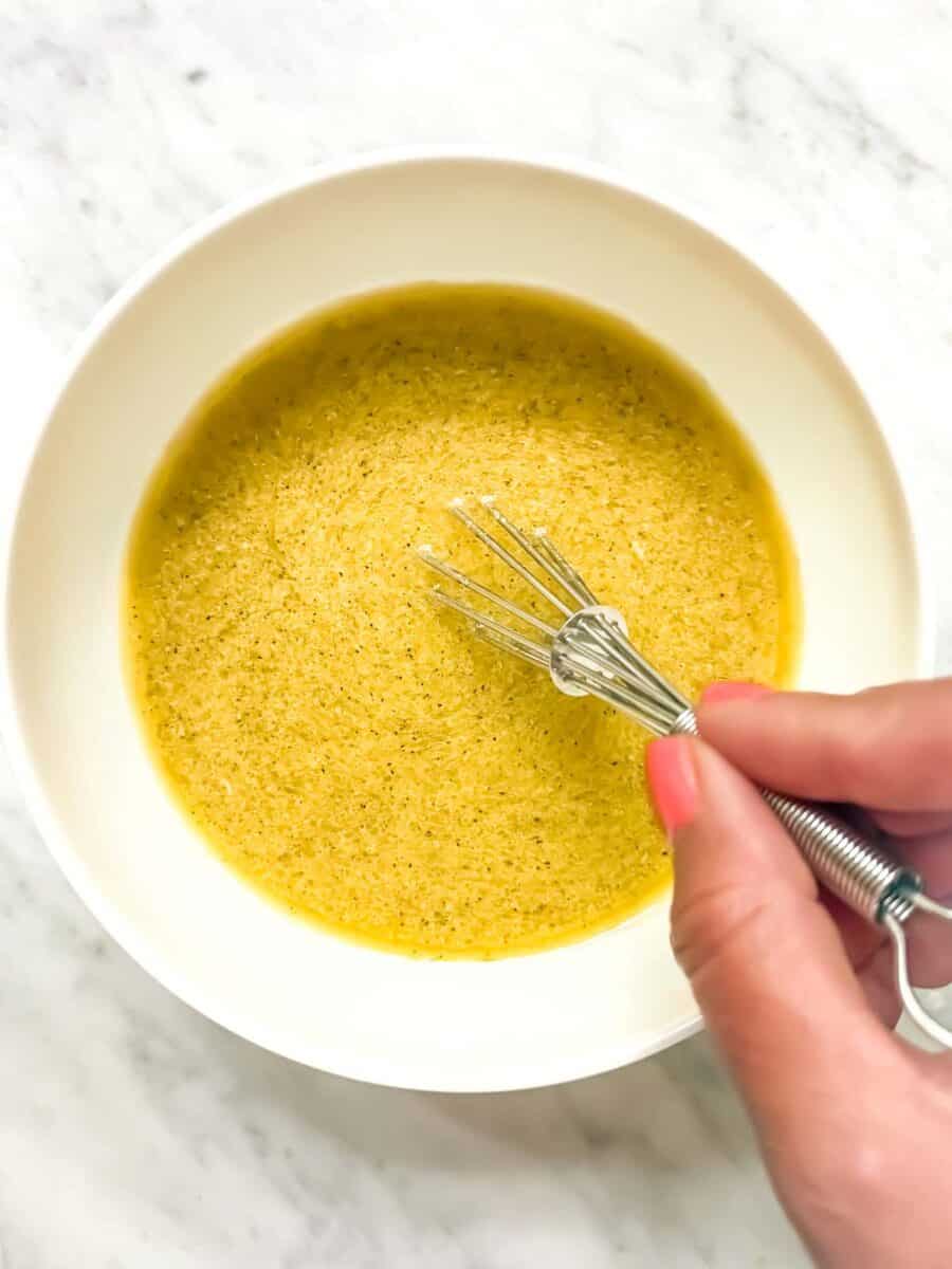 A bright evoo based dressing being whisked in a white bowl