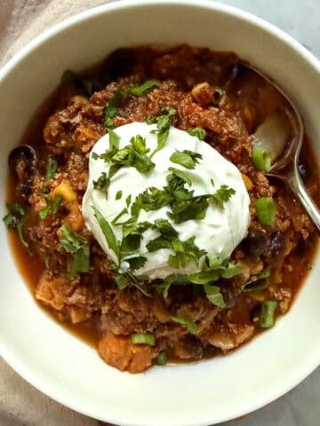 Bowl of vegan sweet potato black bean chili topped with a dollop of vegan sour cream, cilantro, and sliced green onion