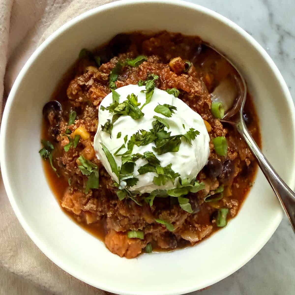 Bowl of vegan sweet potato black bean chili topped with a dollop of vegan sour cream, cilantro, and sliced green onion