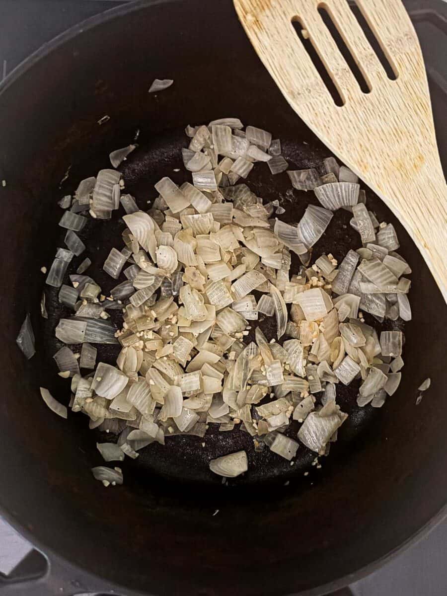 Diced onion and minced garlic sautéing in a black Dutch oven with a wooden spatula
