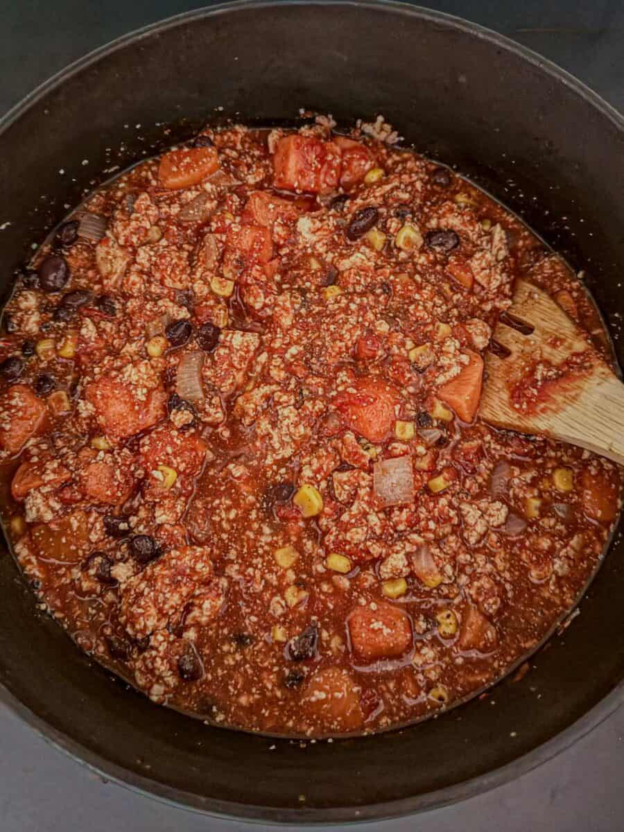 Vegan sweet potato chili simmering in a pot with tofu crumbles, black beans, corn, and sweet potato chunks