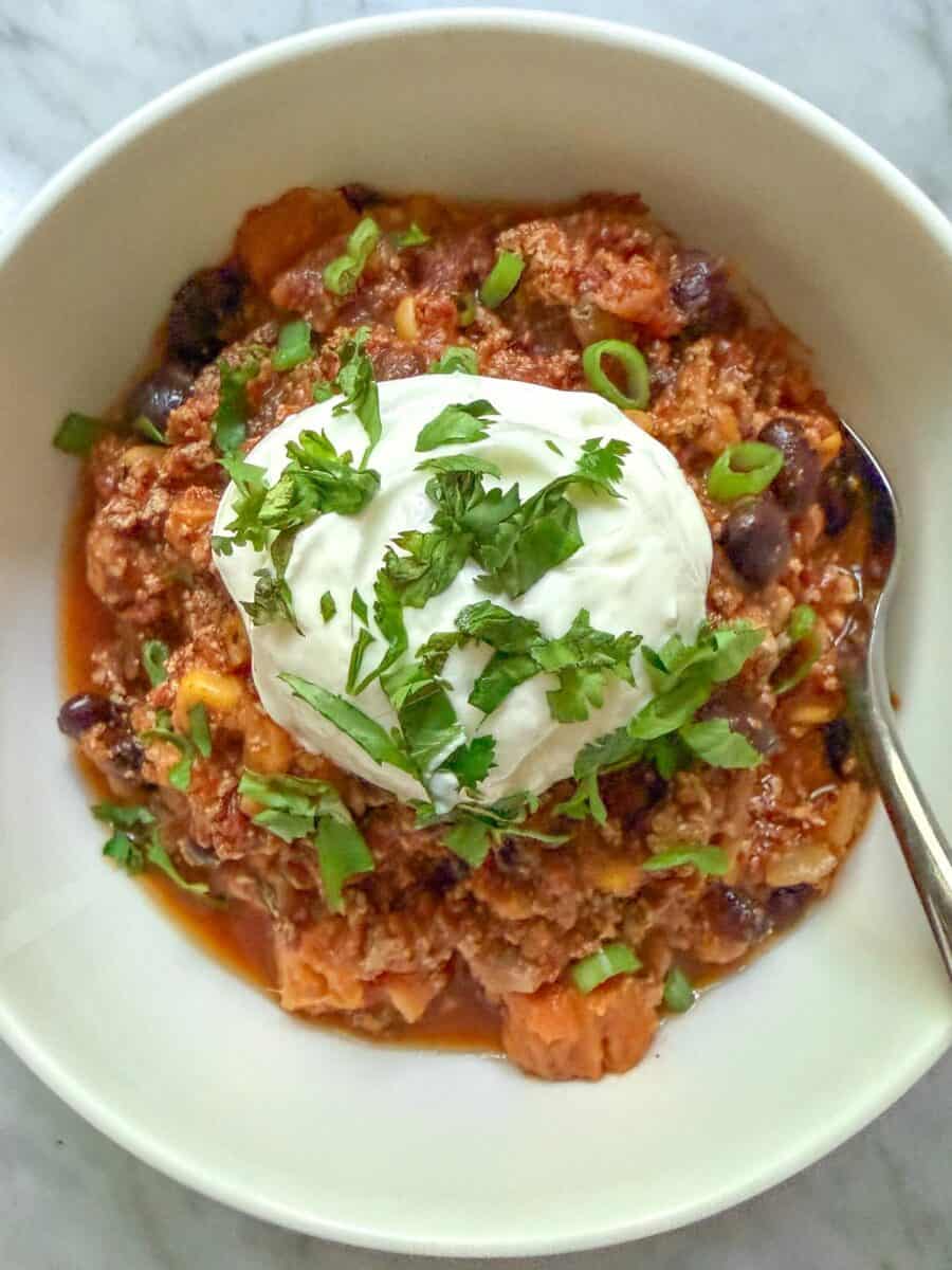 Close-up of a white bowl of vegan sweet potato chili topped with vegan sour cream, cilantro, and green onion