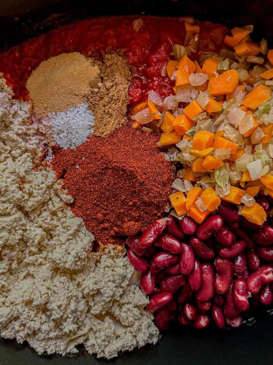 Crumbled tofu, kidney beans, tomatoes, cooked mirepoix, and spices before stirring together.