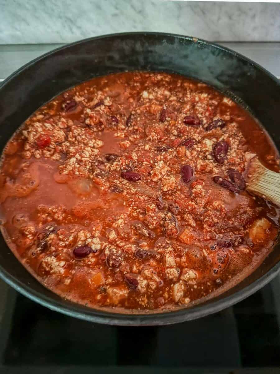 Vegan chili with tofu and kidney beans simmering in a pot on the stove.